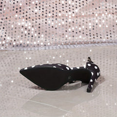 A black stiletto heel sandal with white polka dots, a pointed toe, and an ankle strap.