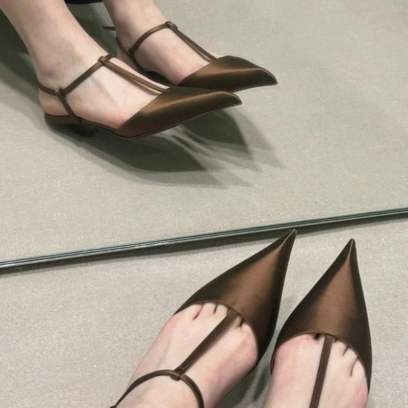 A pair of brown satin pointed-toe t-strap sandals with a low heel shown in a mirror reflection.