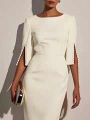 A woman wears an elegant white knee-length dress with split sleeves detailed with pearl buttons.