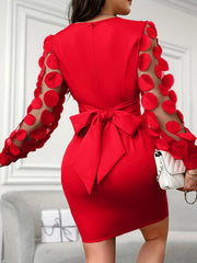 A woman wears a red bodycon dress featuring a large back bow and sheer sleeves with circular accents.