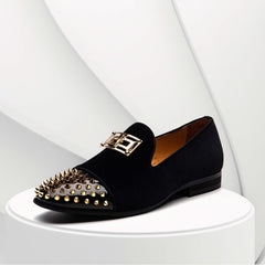 A black velvet loafer with a gold-studded toe cap and a decorative gold metal emblem.