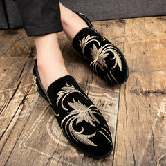 A pair of black slip-on loafers featuring gold floral embroidery on a pointed toe silhouette.