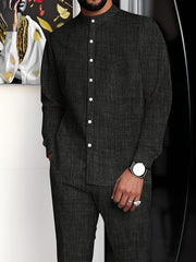 A man wears a dark grey minimalist suit with a stand collar button-up shirt and matching trousers.