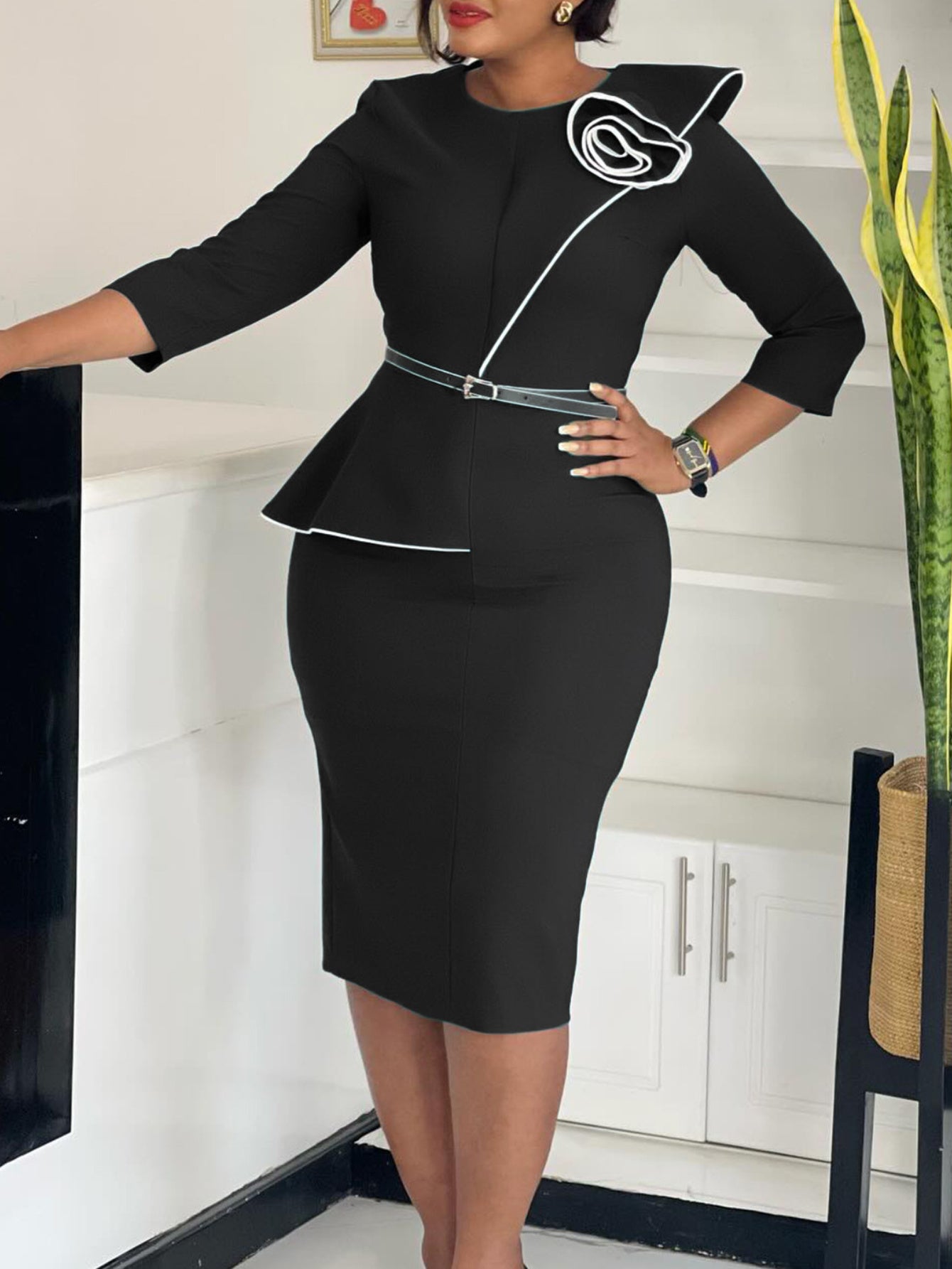 A black bodycon pencil dress with a peplum waist, white trim, and a decorative shoulder flower.