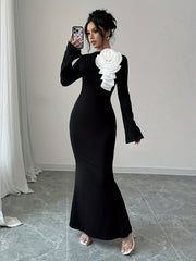A woman wears a black long-sleeve bodycon dress featuring a large white 3D flower applique.