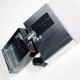 A bottle of 100ML OEM/ODM EDP men perfume, known for its long-lasting fragrance, sits next to its sleek silver and black packaging with the cap nearby on a white surface.