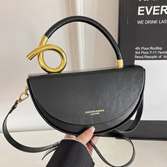 A black, semi-circular saddlebag with a unique golden looped handle and a detachable strap.