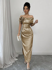 A woman wears a metallic gold off-shoulder bodycon maxi dress with a floral accent and side slit.