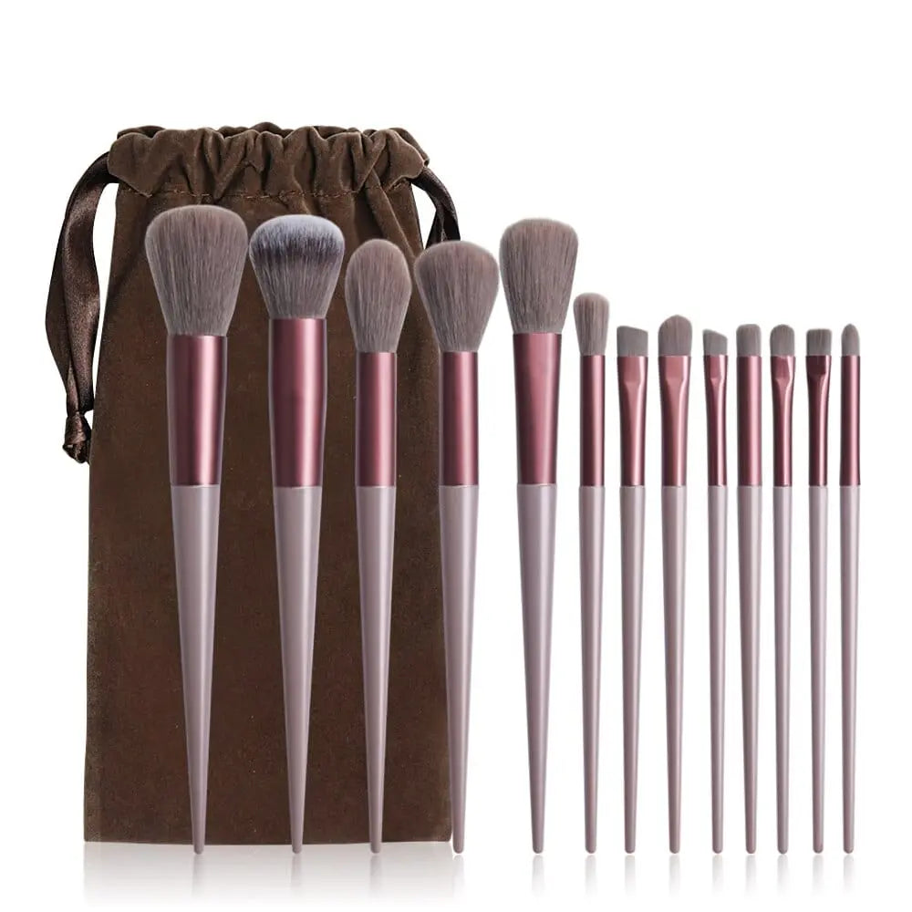The 13 PCS Makeup Brushes Set features metallic pink handles and grey bristles, neatly arranged in a row beside a brown drawstring pouch—perfect for eyeshadow, foundation, blush, and other beauty needs.