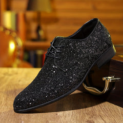 A black glittery lace-up dress shoe with a pointed toe rests on a wooden surface.