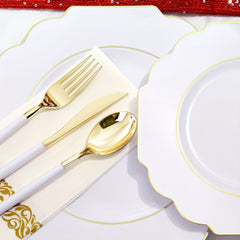 A set of white plastic plates and gold-handled silverware arranged on a decorative napkin.