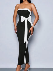 A woman wears a black strapless bodycon gown featuring a white bow detail at the waist.