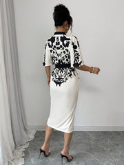 A woman wears a white midi dress with black floral and bird prints, short sleeves, and a waist tie.