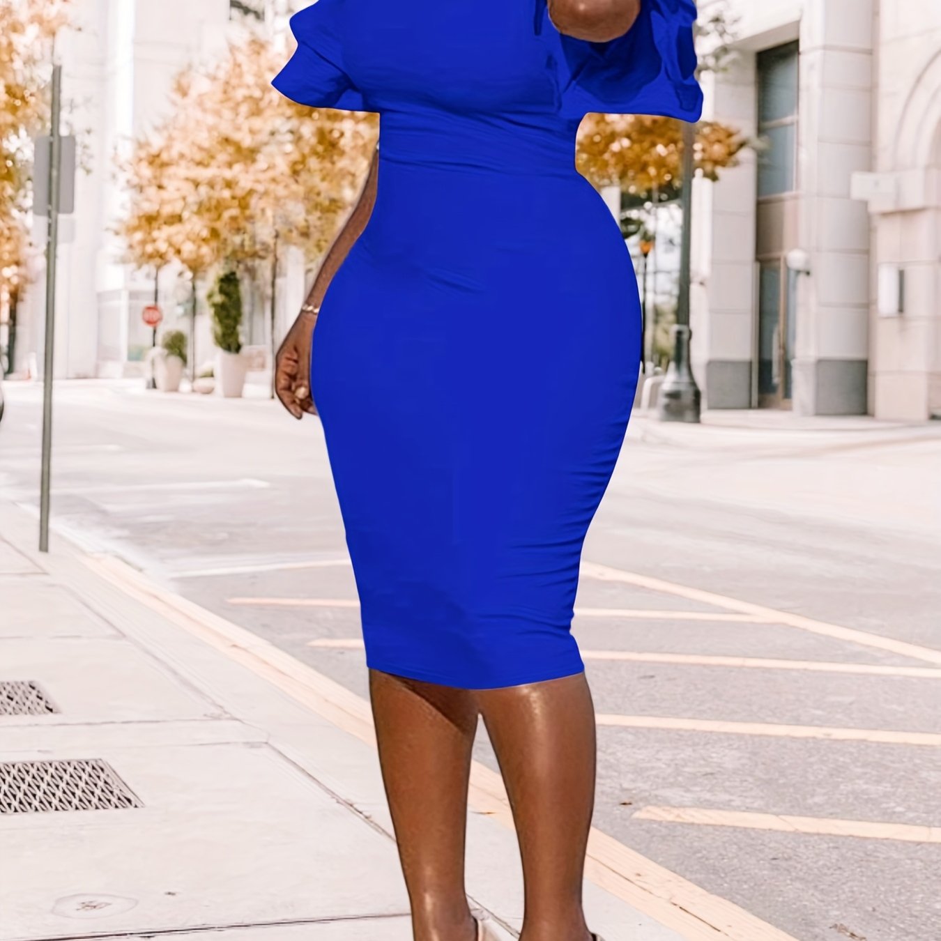 A woman wears a royal blue midi pencil dress featuring short ruffle sleeves and a round neckline.