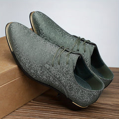 A pair of green glittery lace-up oxford shoes with gold-tone accents on a wooden surface.