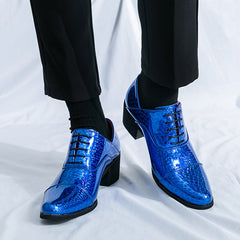 A pair of shiny blue faux leather lace-up dress shoes with a block heel worn with black trousers.