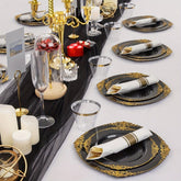 A table setting featuring black and gold plastic plates, pre-rolled napkins, and gold cutlery.