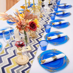 A table setting featuring blue plastic plates with gold rims, matching blue cups, and pre-rolled napkins with gold cutlery.