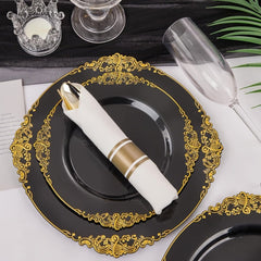 A black plastic dinner plate with an ornate gold rim, featuring a pre-rolled napkin and cutlery.