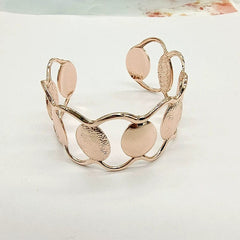A rose gold cuff bracelet featuring an open design with alternating smooth and textured circles.