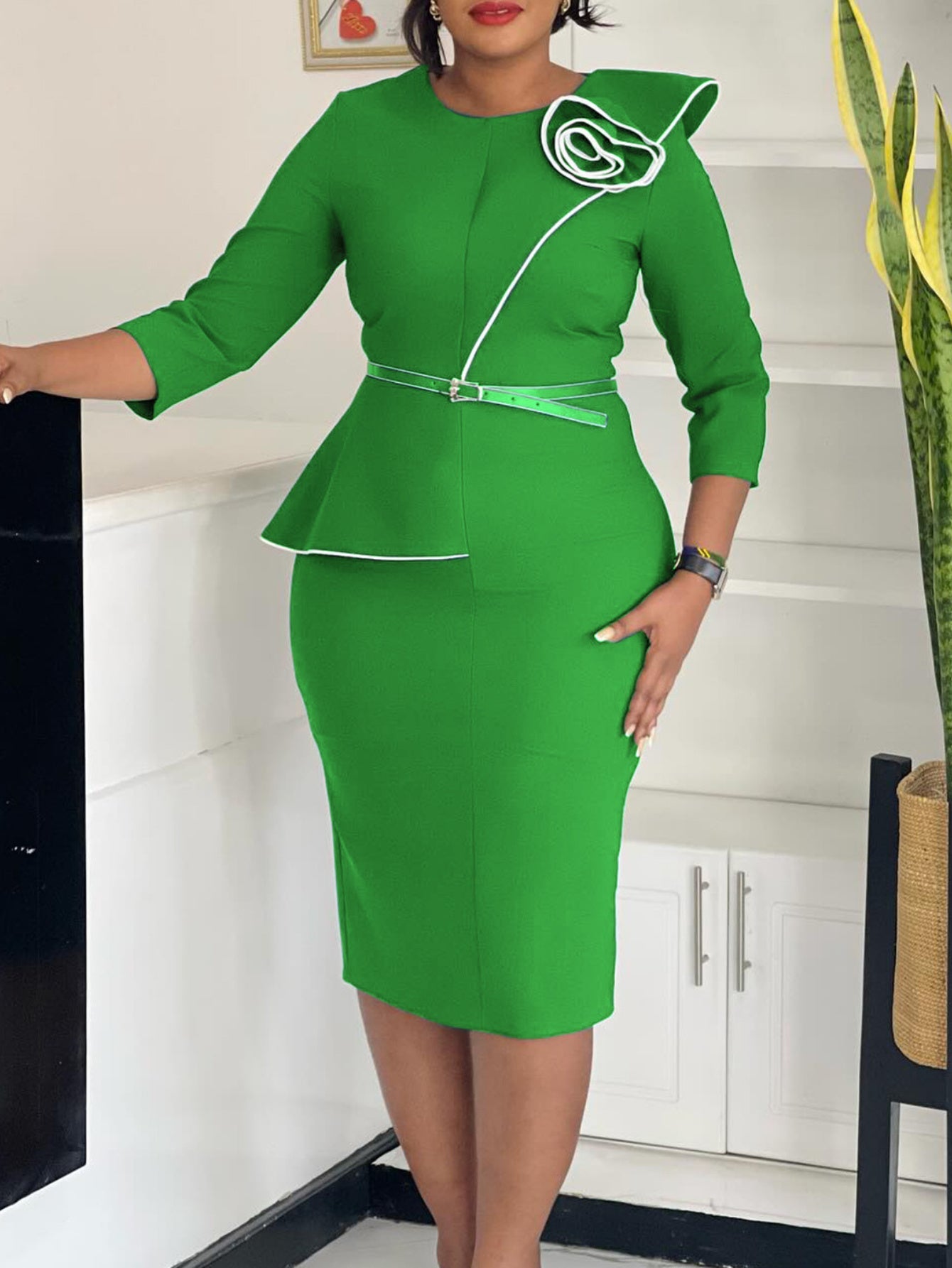 A bright green knee-length pencil dress with a peplum waist, white trim, and a floral shoulder detail.