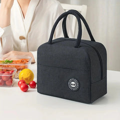 A black, rectangular insulated lunch bag with a panda logo patch sits on a white table.