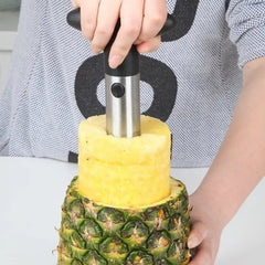 A person uses a stainless steel pineapple slicer to core and peel a fresh pineapple.