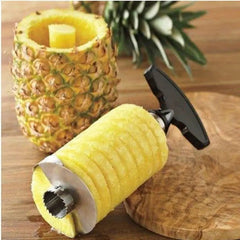 A stainless steel pineapple slicer and corer tool with a black handle next to a cored pineapple.