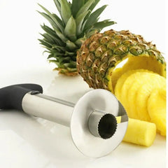 A stainless steel pineapple slicer and corer tool sits next to a sliced pineapple.
