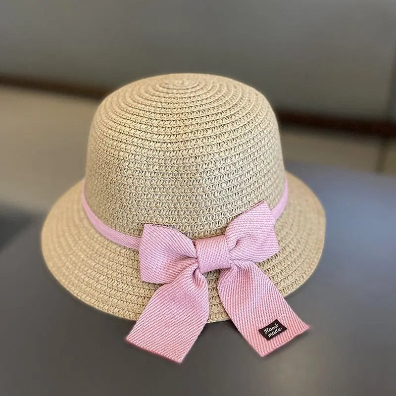 This unisex baby sun hat for ages 2-8 features a beige straw design with a wide brim, light pink ribbon, and large pink bow, plus a small black tag—part of the Summer Straw Bag Cap Set for girls' travel and beach sun protection.