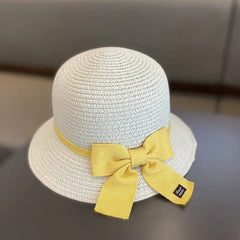 The 2-8 Years Kids Sun Hat is a light floral straw hat with a wide brim and large yellow ribbon bow, perfect for sun protection. Shown on a neutral background, it's ideal for girls’ summer travel or the beach.