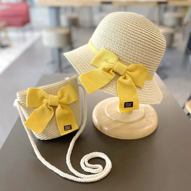A kids' sun hat and matching straw bag set, both with yellow bows, for ages 2-8. The summer accessory set offers sun protection—perfect for travel or the beach. Displayed on a table with a blurred background.