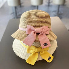 Two kids' summer straw hats from the Sun Hat & Bag Set are stacked on a table. The top hat is light brown with a pink bow, the bottom is beige with a yellow bow, and both have small black tags attached. Suitable for ages 2-8 years.