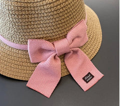 The 2-8 Years Kids Sun Hat is a brown floral straw hat with a pink ribbon bow and "Hand made" black tag, perfect for travel and sun protection. Ideal for girls in summer, this beach fisherman hat is part of a stylish cap set.