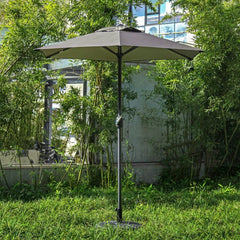 A brown outdoor patio umbrella stands on a circular base in a grassy garden setting.