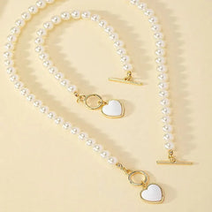 A two-piece jewelry set featuring a pearl necklace and bracelet with gold heart pendants.