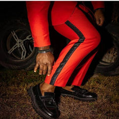 A person wears a red slim-fit suit with black side stripes and black leather loafers.