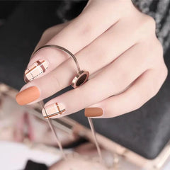 A hand displays nails with a matte brown and plaid nail art design.
