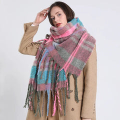 A woman wears a long, thick plaid scarf in shades of pink, blue, and grey with fringed edges.