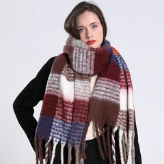A woman wears a long, thick, plaid cashmere scarf with fringe in shades of brown, red, and blue.