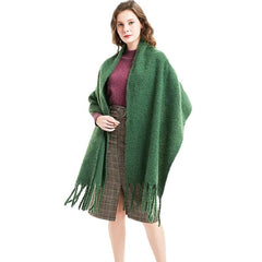 A woman wears a long, thick green cashmere shawl with fringe edges over a plaid skirt.