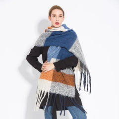 A woman wears a long, thick plaid scarf featuring blue, orange, white, and grey tones with tassels.