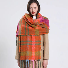 A woman wears a long, thick, orange and green plaid cashmere scarf with fringe tassels.