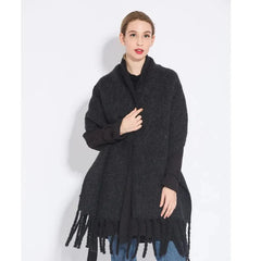 A woman wears a long, dark gray textured cashmere shawl with fringe trim.