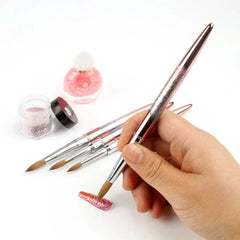A hand holds a professional Kolinsky sable acrylic nail brush with a metallic gradient handle.
