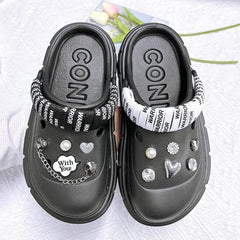 A pair of black platform clogs decorated with various charms and a branded fabric heel strap.