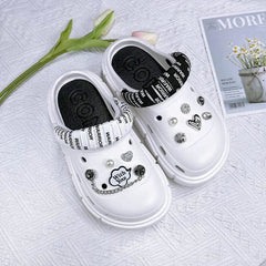 A pair of white platform clogs decorated with various charms and a black and white strap.