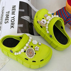 A pair of lime green platform clogs decorated with pearl chains and floral charms.