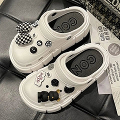 A pair of white platform clogs decorated with black and white charms on a black surface.