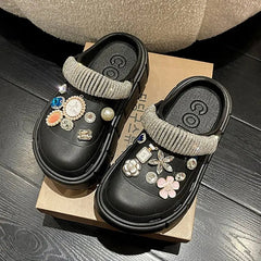 A pair of black platform clogs decorated with various rhinestone charms and a crystal strap.